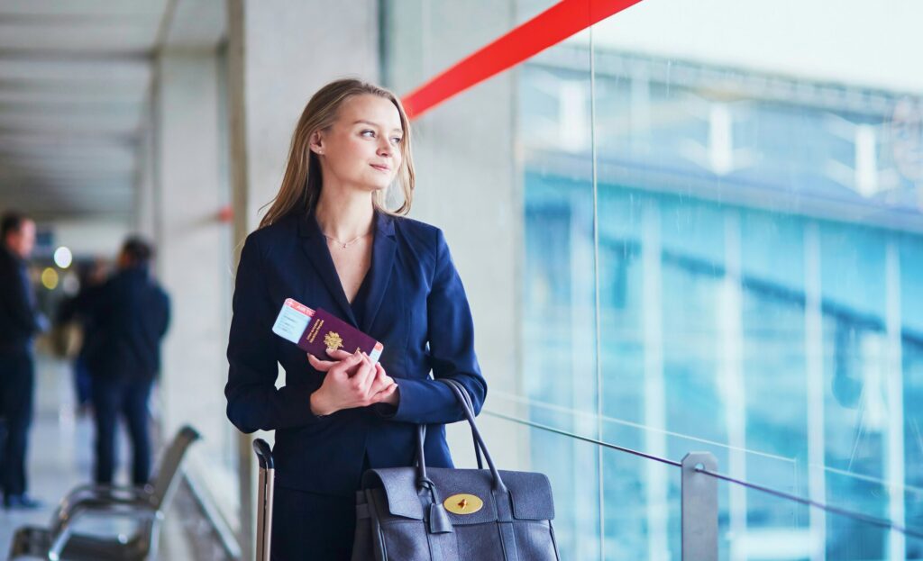 Blond woman in business suit with passport in her hands staring out the window at an airport